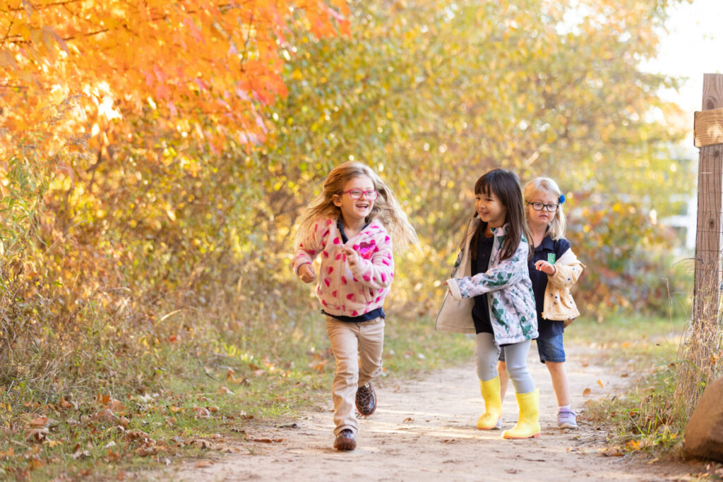 Three joyful girls run through a vibrant autumn landscape filled with colorful leaves.