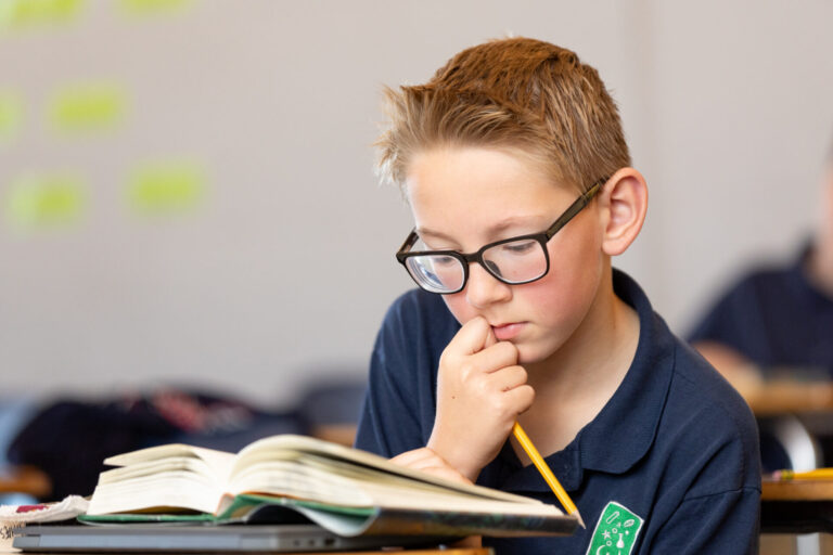 Young boy reading intently in a classroom, showcasing focus and academic engagement.