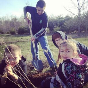 students pose for the camera while young male shovels soil.