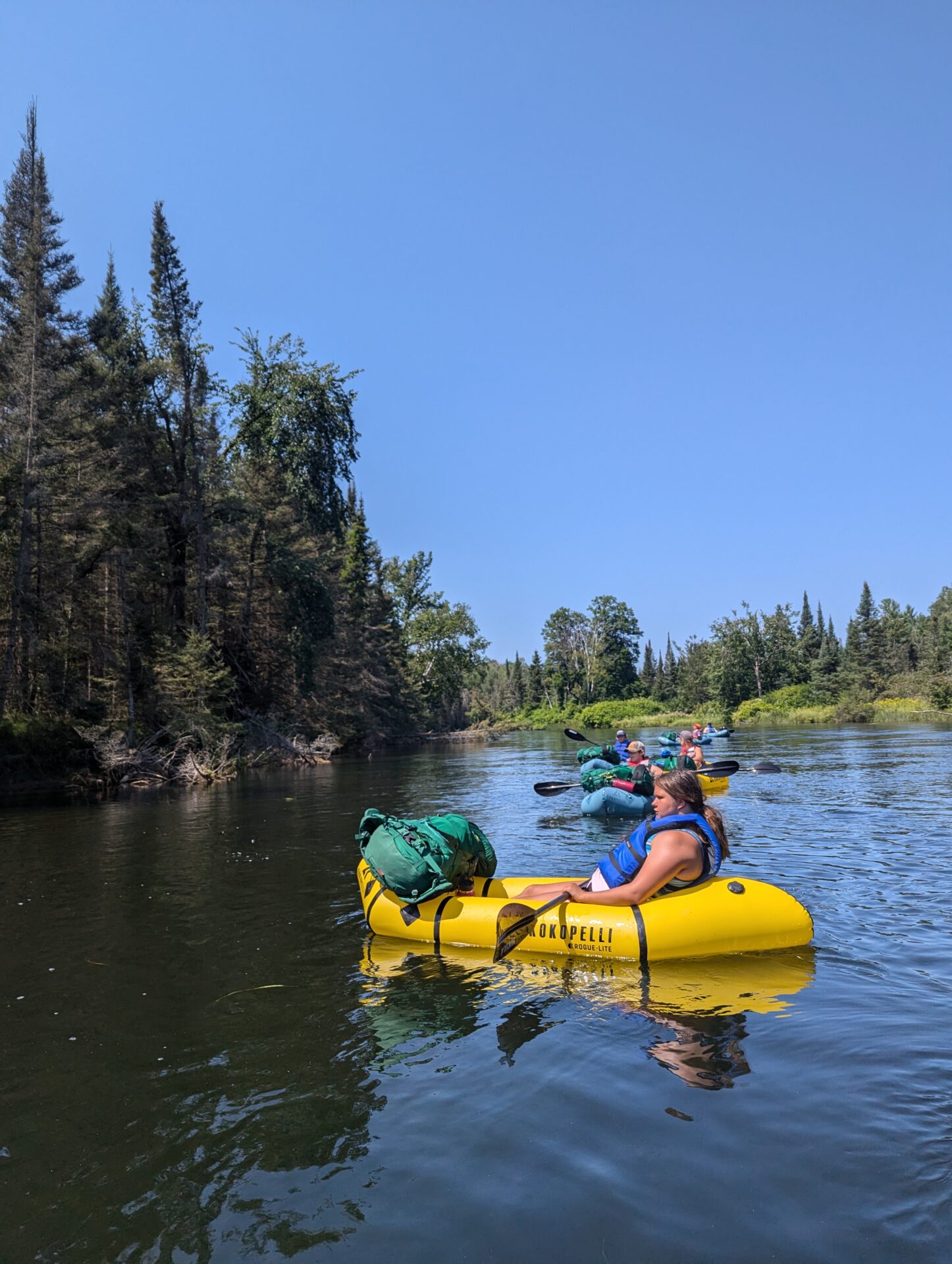 Colorful kayaks on a serene river, surrounded by lush trees under a clear blue sky.