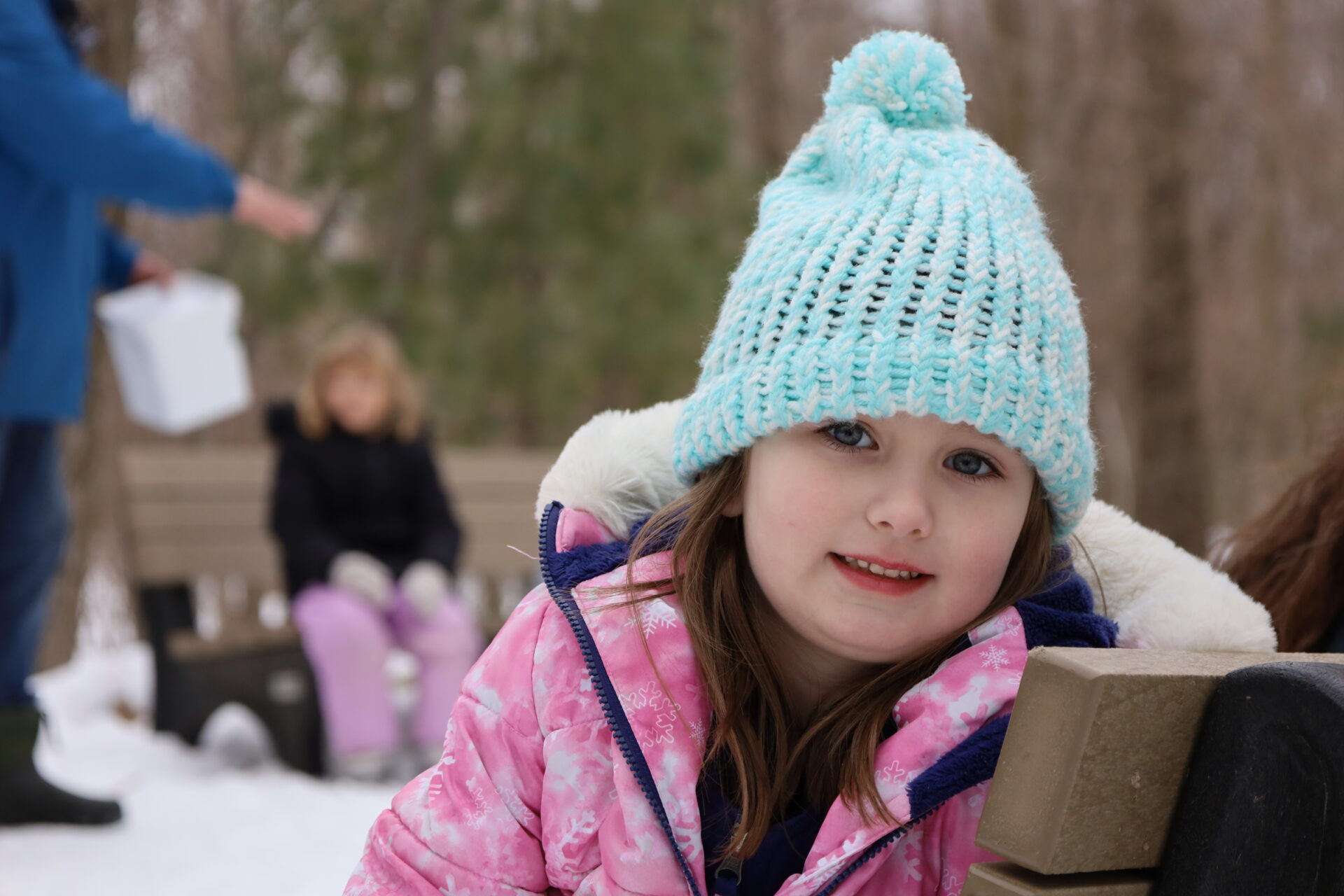 Young girl in winter attire smiling in a snowy landscape, enjoying outdoor play.